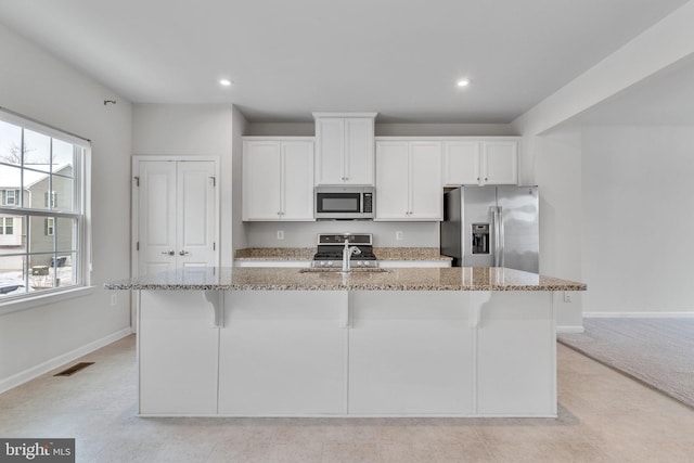 kitchen with stainless steel appliances, light stone counters, a kitchen island with sink, and white cabinets