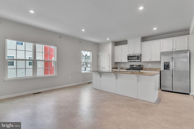 kitchen with visible vents, stainless steel appliances, a center island with sink, and white cabinets