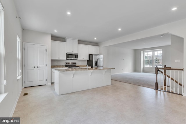 kitchen with light stone counters, a center island with sink, appliances with stainless steel finishes, open floor plan, and white cabinetry