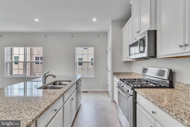 kitchen featuring light stone counters, appliances with stainless steel finishes, white cabinetry, a sink, and plenty of natural light