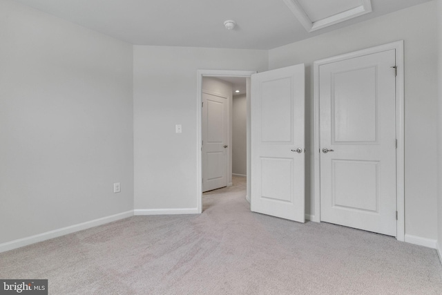 unfurnished bedroom featuring baseboards, attic access, and light colored carpet