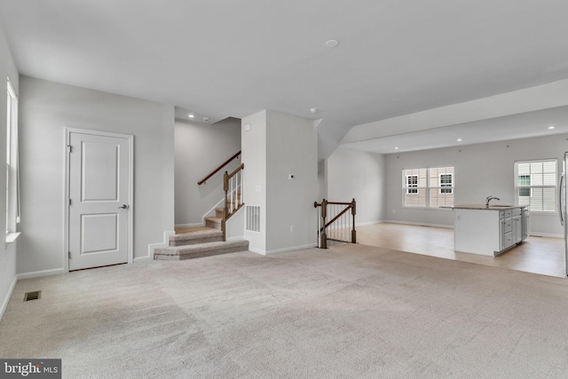 unfurnished living room with light colored carpet, visible vents, a sink, and recessed lighting