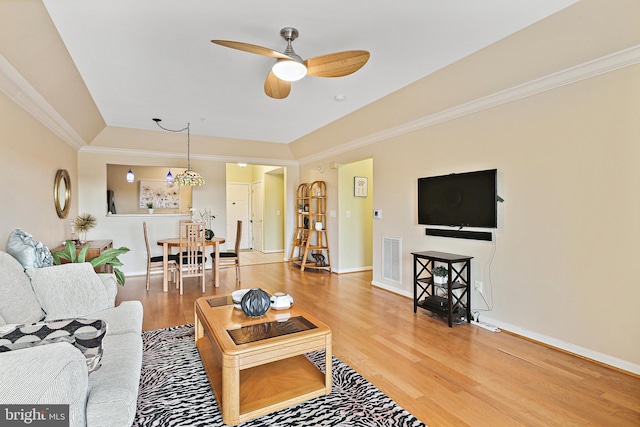 living room with baseboards, wood finished floors, visible vents, and crown molding