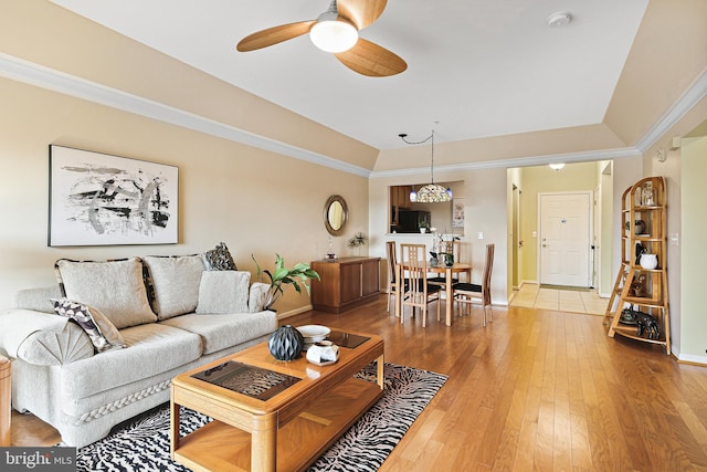 living area featuring a tray ceiling, ornamental molding, a ceiling fan, wood finished floors, and baseboards