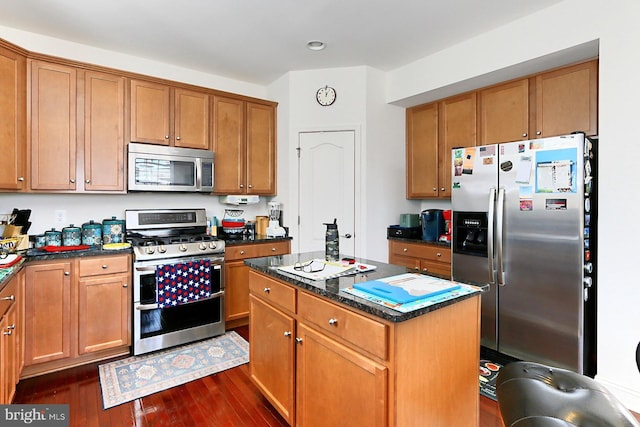 kitchen with appliances with stainless steel finishes, a center island, brown cabinets, and dark wood-type flooring