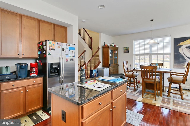 kitchen featuring stainless steel fridge, dark wood-style flooring, a center island, dark stone countertops, and decorative light fixtures