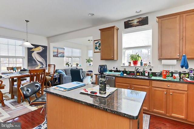 kitchen with decorative light fixtures, dark wood-type flooring, a kitchen island, a sink, and dark stone countertops