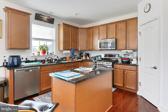 kitchen with dark stone counters, dark wood-style floors, a center island, stainless steel appliances, and a sink