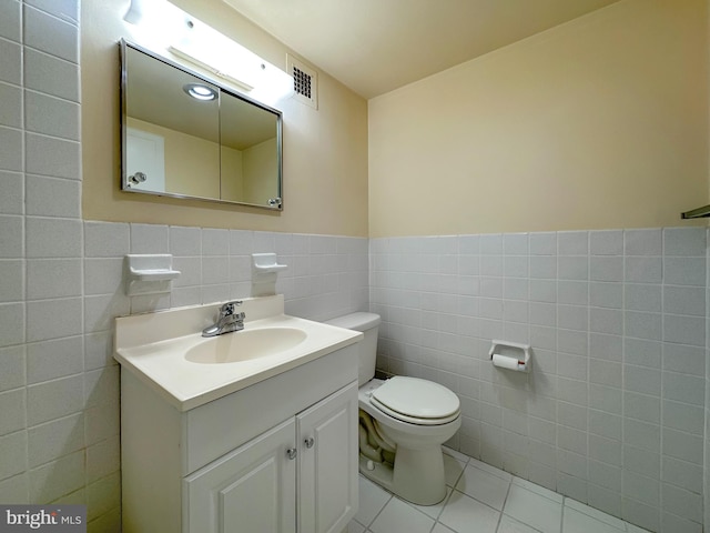 half bath with tile patterned flooring, toilet, vanity, visible vents, and tile walls