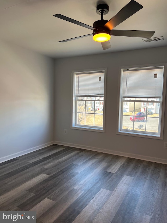 unfurnished room with dark wood-style floors, visible vents, and baseboards