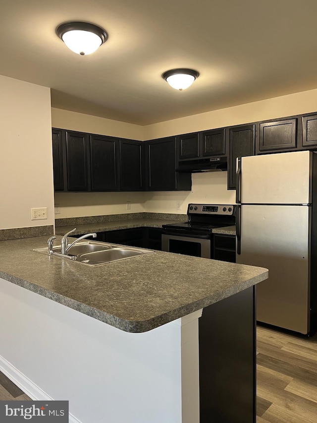 kitchen featuring a peninsula, dark countertops, appliances with stainless steel finishes, and a sink