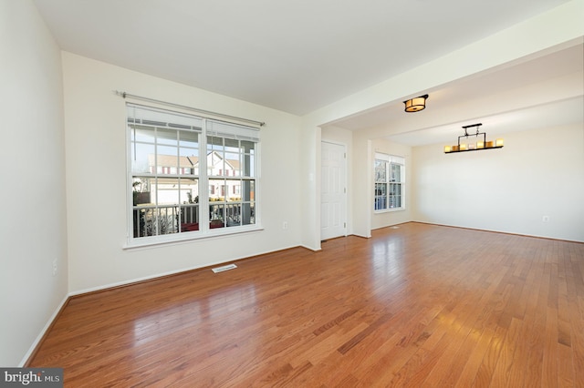 spare room featuring a chandelier, a wealth of natural light, and wood-type flooring