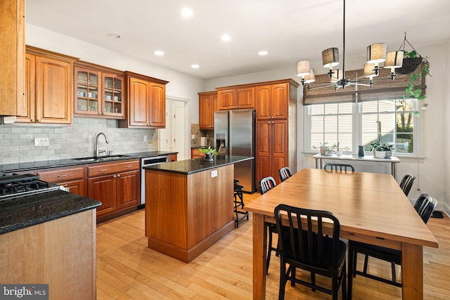 kitchen featuring glass insert cabinets, a kitchen island, appliances with stainless steel finishes, light wood-style flooring, and a sink