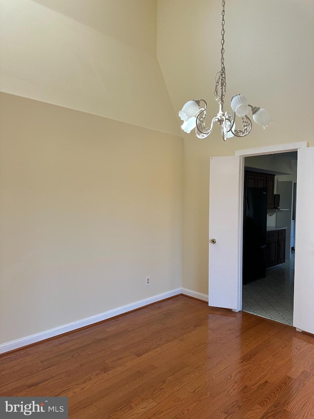 empty room with vaulted ceiling, a notable chandelier, wood finished floors, and baseboards