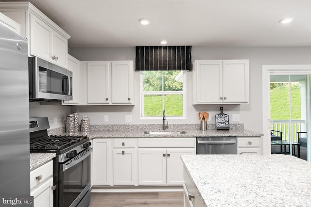 kitchen with white cabinets, light stone counters, appliances with stainless steel finishes, a sink, and recessed lighting