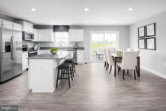 kitchen featuring appliances with stainless steel finishes, dark stone countertops, a center island, a kitchen bar, and white cabinetry