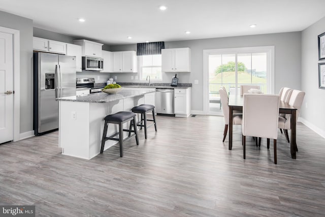 kitchen with appliances with stainless steel finishes, a kitchen breakfast bar, dark stone countertops, a center island, and white cabinetry