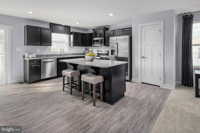 kitchen with a kitchen island, appliances with stainless steel finishes, a breakfast bar, dark cabinets, and light stone countertops