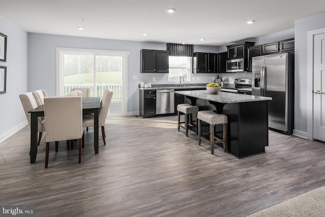 kitchen featuring a kitchen breakfast bar, dark cabinets, a center island, light stone countertops, and stainless steel appliances