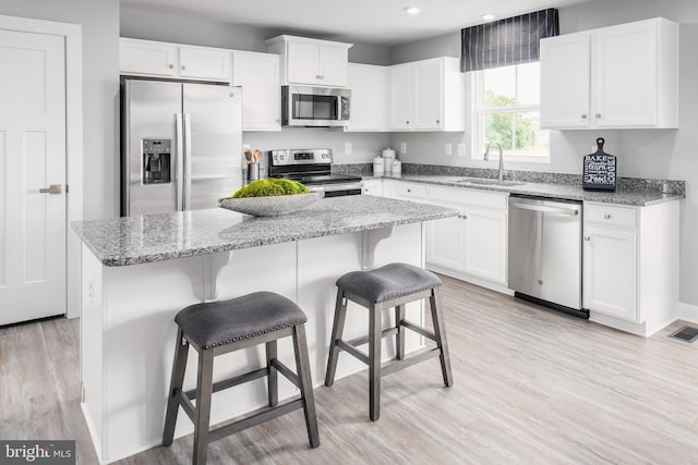 kitchen featuring appliances with stainless steel finishes, white cabinets, a sink, and a center island