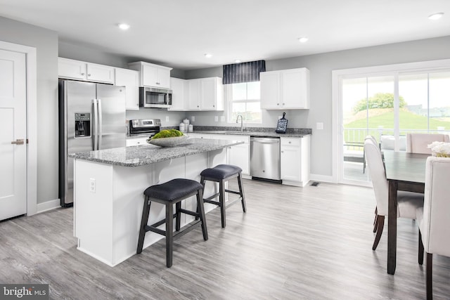 kitchen featuring stainless steel appliances, stone countertops, white cabinets, a kitchen island, and a kitchen bar