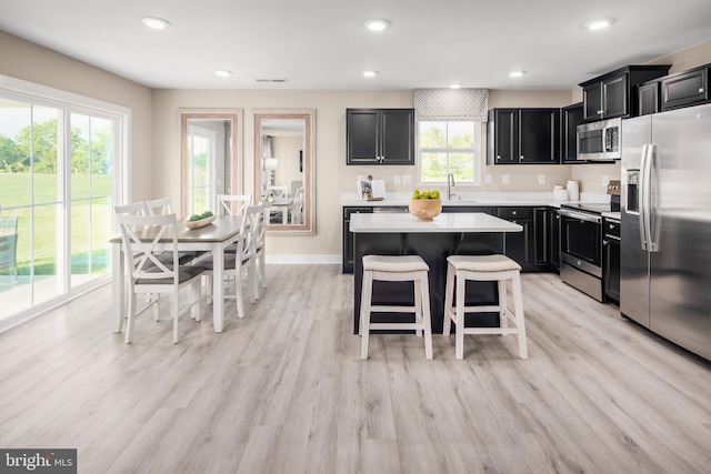 kitchen with dark cabinets, a kitchen island, a kitchen breakfast bar, light countertops, and appliances with stainless steel finishes