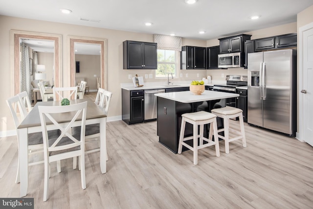 kitchen with a kitchen island, appliances with stainless steel finishes, a kitchen breakfast bar, light countertops, and a sink