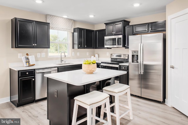 kitchen with a sink, light countertops, appliances with stainless steel finishes, dark cabinetry, and a kitchen bar