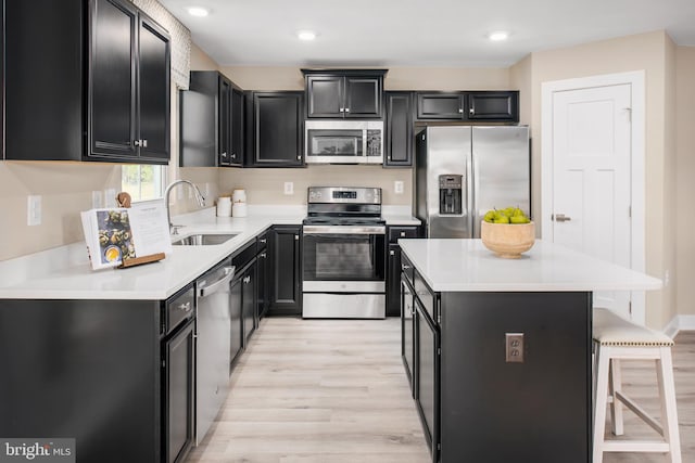 kitchen featuring appliances with stainless steel finishes, light countertops, dark cabinetry, a kitchen bar, and a sink