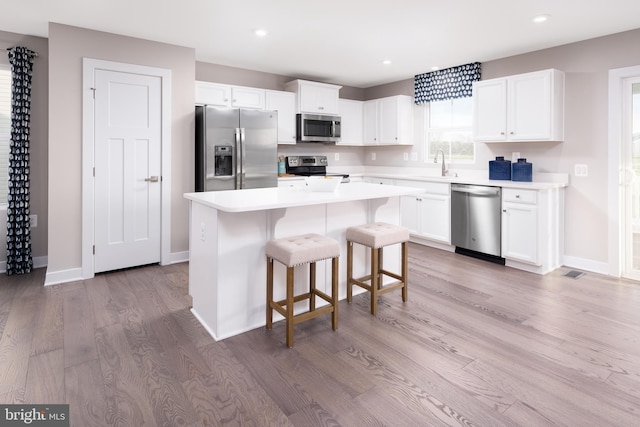 kitchen with stainless steel appliances, a kitchen island, light countertops, and white cabinets