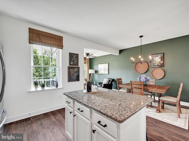 kitchen featuring dark wood-type flooring, light stone countertops, white cabinets, decorative light fixtures, and a center island