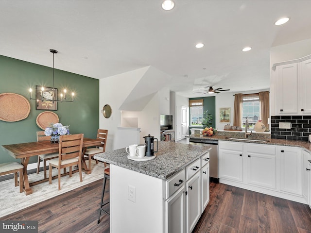 kitchen featuring white cabinetry, a center island, sink, dishwasher, and dark stone countertops