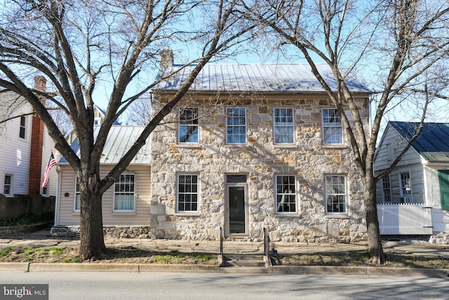 colonial home with metal roof, stone siding, a chimney, and a standing seam roof