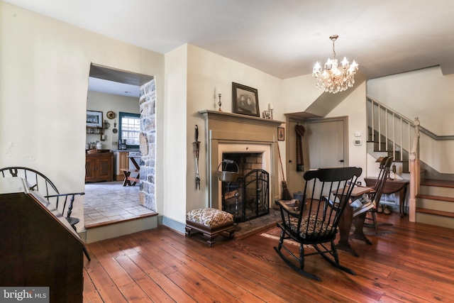 living area featuring hardwood / wood-style flooring, stairway, a notable chandelier, and a fireplace with raised hearth