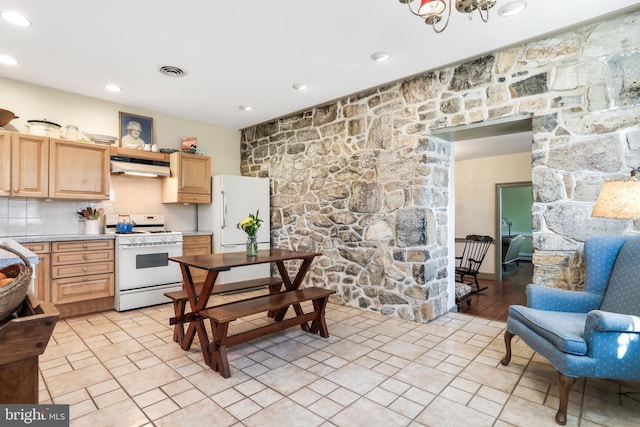 kitchen with visible vents, backsplash, light brown cabinets, under cabinet range hood, and white appliances