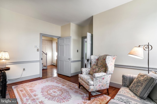 sitting room with stairway, a baseboard heating unit, baseboards, and wood finished floors