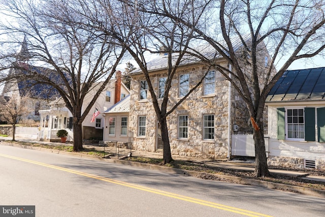 view of front of property with stone siding, metal roof, a standing seam roof, and fence