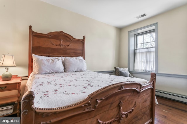 bedroom featuring visible vents, baseboard heating, and wood finished floors