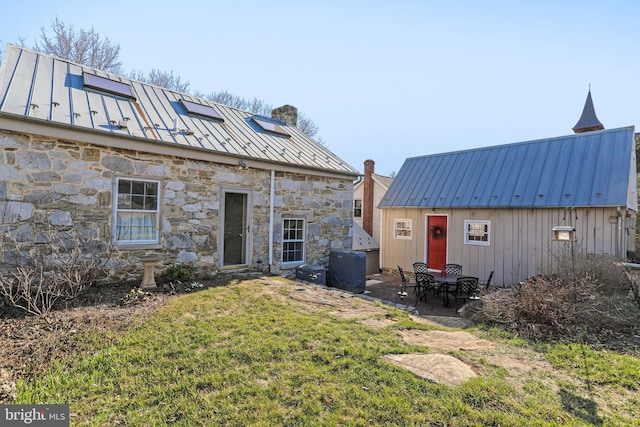 rear view of house featuring metal roof, stone siding, a chimney, and a standing seam roof