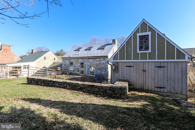 back of house with fence, a chimney, an outdoor structure, stone siding, and a lawn