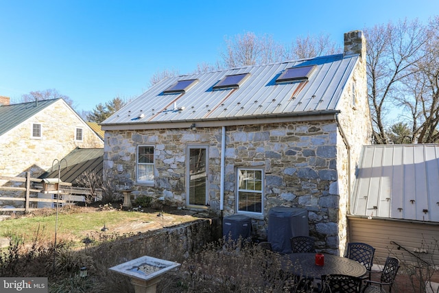 rear view of house featuring fence, a chimney, metal roof, stone siding, and a standing seam roof