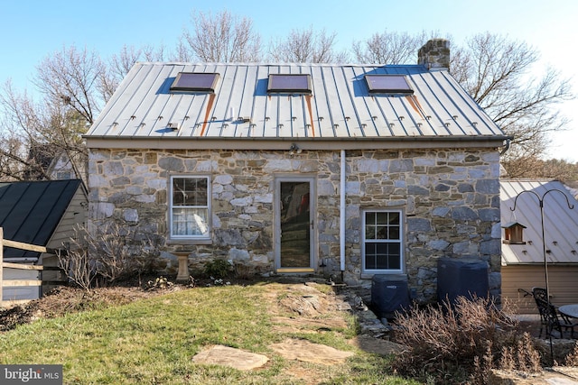 rear view of property with metal roof, stone siding, a chimney, and a standing seam roof