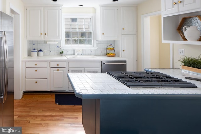 kitchen with a sink, white cabinets, appliances with stainless steel finishes, tile counters, and light wood finished floors