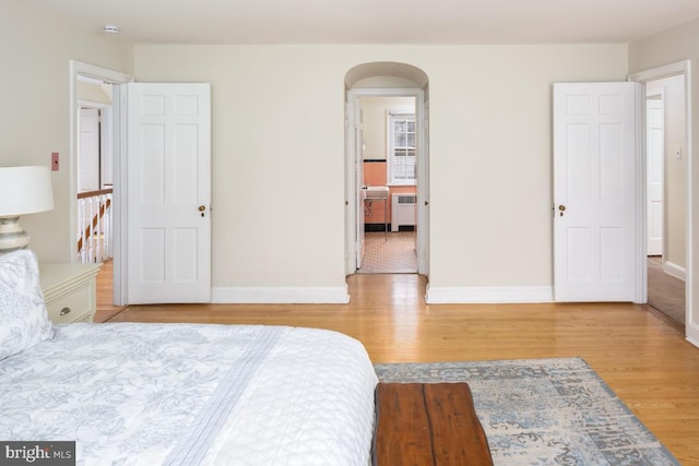 bedroom with radiator, baseboards, arched walkways, and wood finished floors