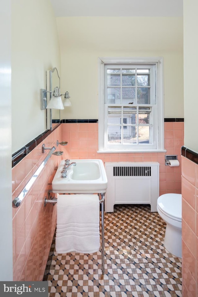 half bath featuring tile walls, toilet, radiator heating unit, wainscoting, and vanity