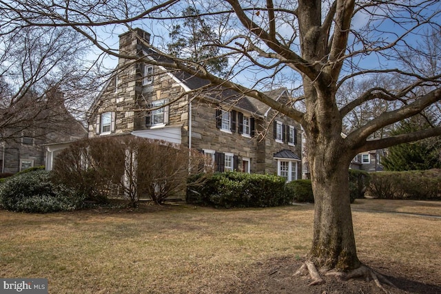 view of side of property with stone siding, a chimney, and a lawn