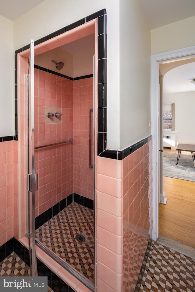 full bathroom with radiator heating unit, a stall shower, wainscoting, and tile walls