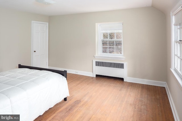 unfurnished bedroom featuring lofted ceiling, light wood-style floors, radiator heating unit, and baseboards