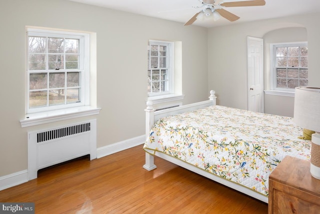 bedroom featuring a ceiling fan, radiator heating unit, baseboards, and wood finished floors