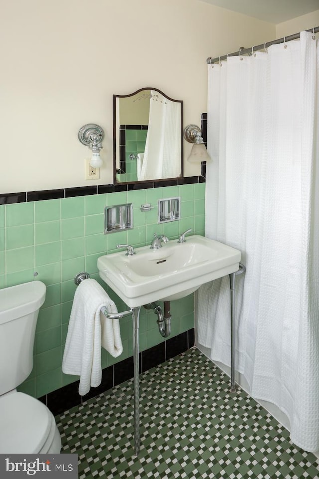 full bath with curtained shower, toilet, a wainscoted wall, a sink, and tile walls